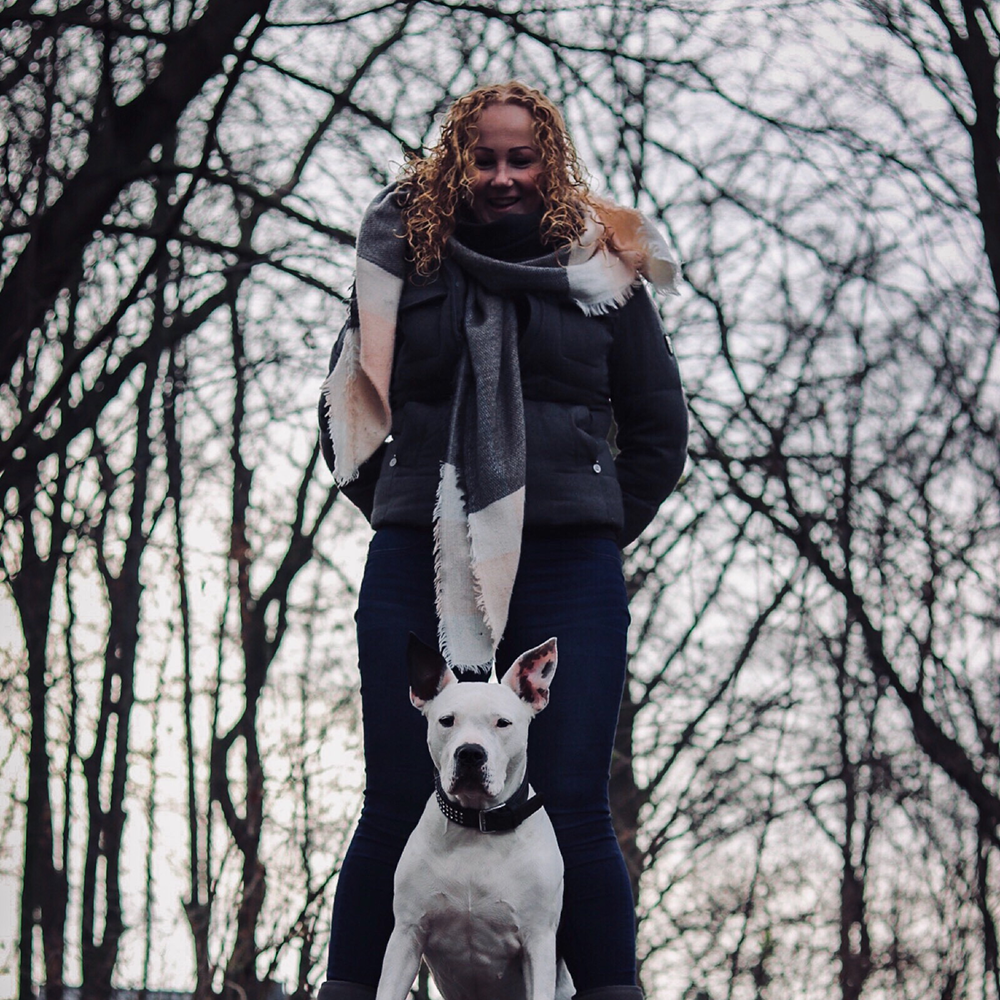 Jana steht mit ihrem weißen Hund in einem winterlichen Wald